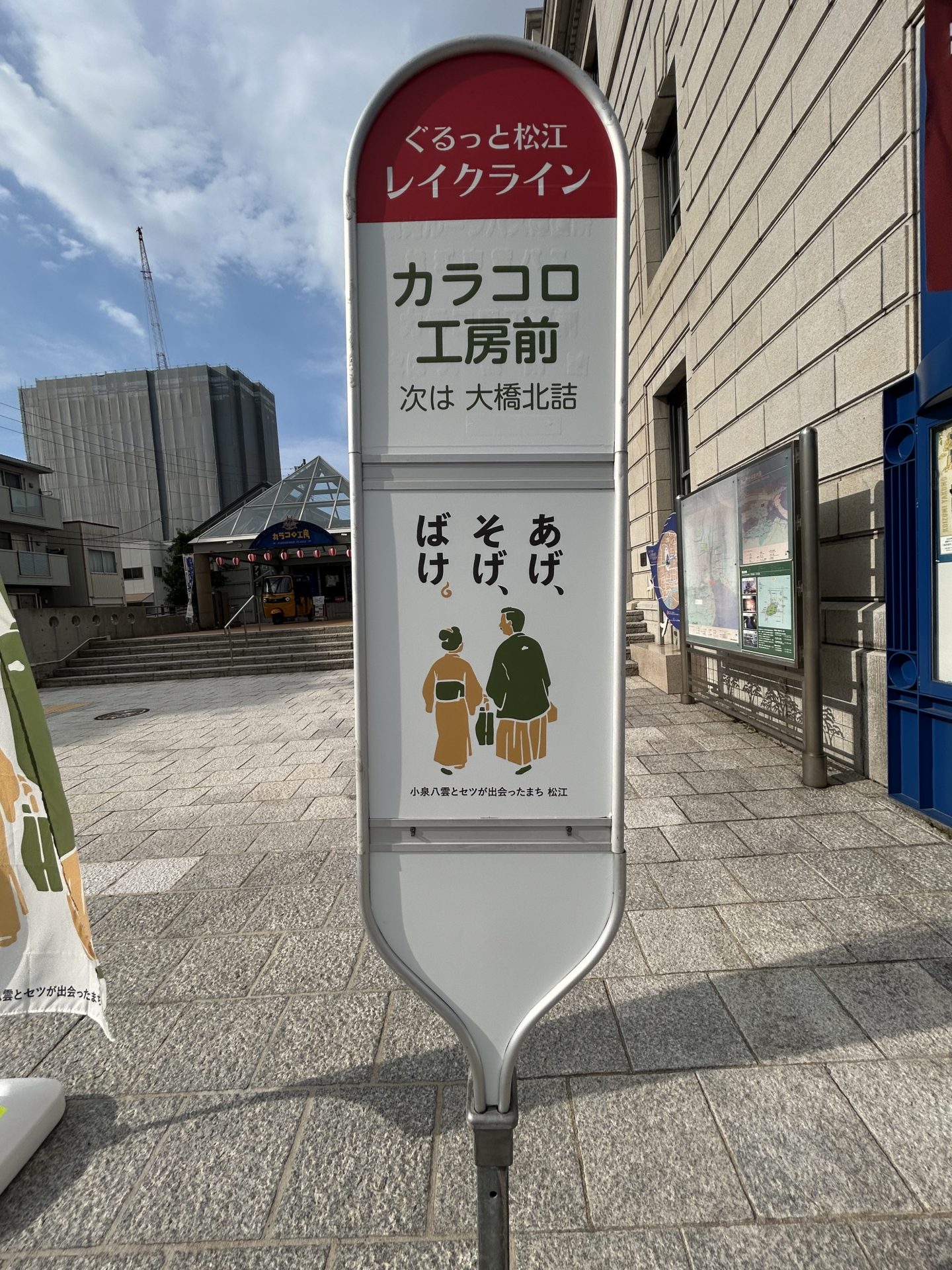 石造りの昔の銀行の建物・カラコロ工房の脇に立つバス停 縦書きで あげ・そげ・ばけと書かれている